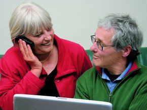 Couple de personnes âgées devant un ordinateur portable se regardant pendant qu'elle parle au téléphone